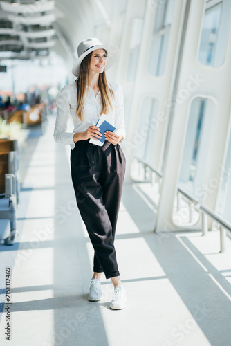 Young woman in stylish hat and white shirt holding passports and boarding passes at airport terminal