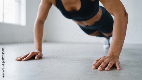 Young athletic woman doing pushups on concrete floor in bright fitness studio