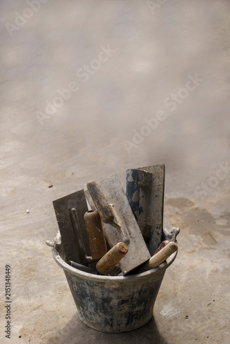Trowel for construction tool set inside bucket for masonry plastering on concrete cement floor, equipment for builder repair work-vertical image.