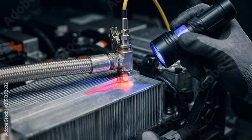 Technician uses a specialized ultraviolet flashlight to inspect the cooling system of an electric car.