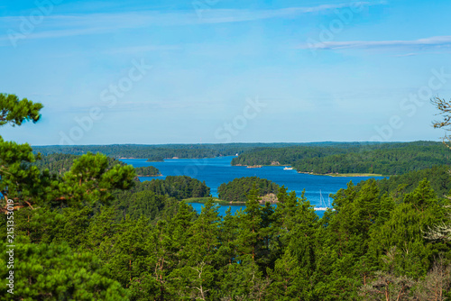 Zoom in aerial view of a single green island surrounded by blue Baltic Sea in Finnish Archipelago