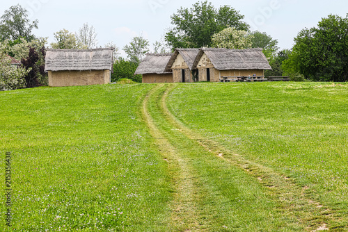Dirt Track Through Green Meadow Leading to Thatched Cottages in Rural Countryside, Sopot culture, Vinkovci, Croatia