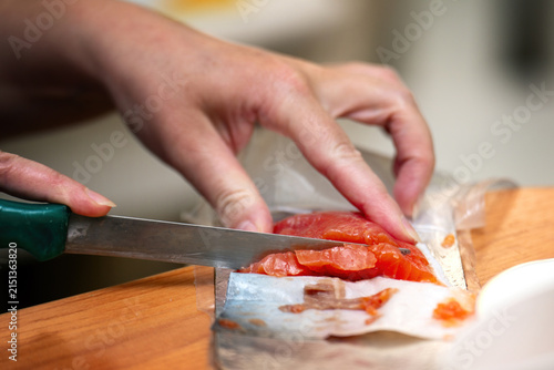 Girl's hand slicing salted red salmon into pieces for breakfast with a vintage knife at home. Morning meal preparation.