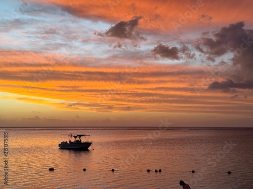 Boat on calm sea at fiery striped sunset sky