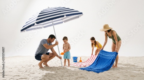 A family setting up their beach umbrella and towels on a sunny day at the shore. White background