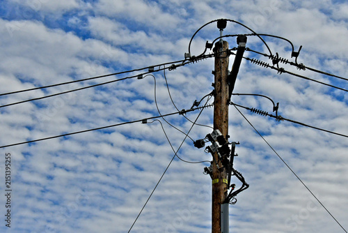 Retrofitted power pole with new jumper cables, cutout fuses and guy wires backed by parallel rows of cumulus clouds