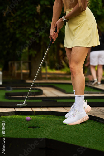 Obraz na plátně Girl holding a metal putter to hit a bright pink ball during an outdoor mini gol