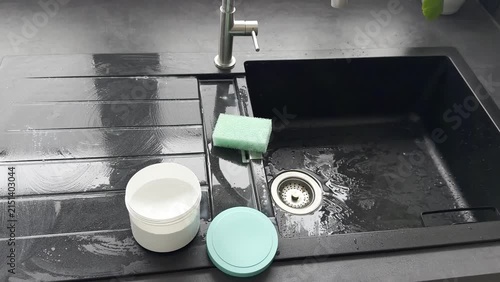 Cleaning process in modern kitchen sink with cleaning product and green sponge