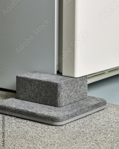 Grey felt door stopper block placed on a carpet floor against a door and wall corner detail