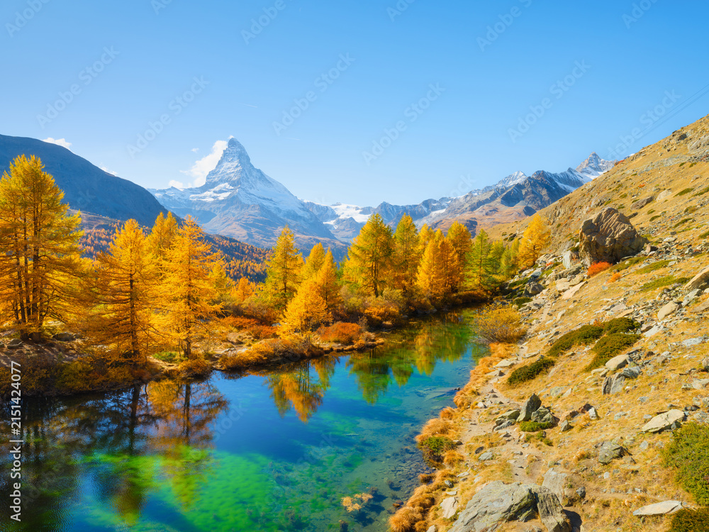 Obraz premium Matterhorn mountain in Switzerland reflects in a calm alpine lake. Scenic mountain landscape with colorful autumn trees under a clear sky in daytime.