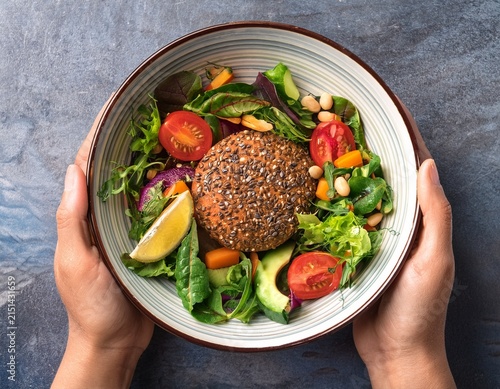 hands holding bowl of vegetarian burger salad with fresh ingredients