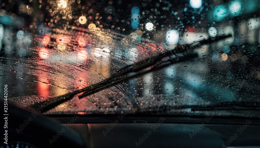 Fototapeta premium Medium shot of a rainy night windshield with raindrops blurring city lights windshield wipers in motion clearing the light drizzle for a cinematic street view.