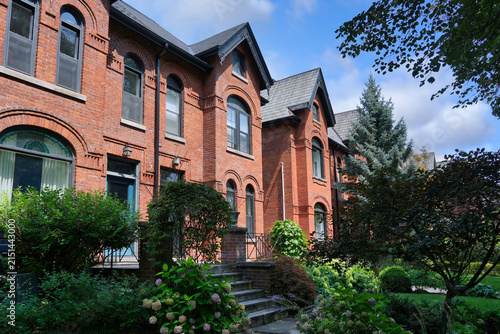 Foto Old urban brick semi-detached houses with shady front yards with trees and bushe