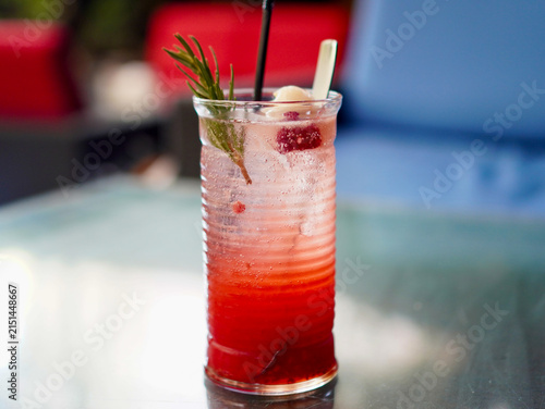 A glass of layered iced lychee raspberry mocktail garnished with fresh rosemary sprig, whole lychee, and berries