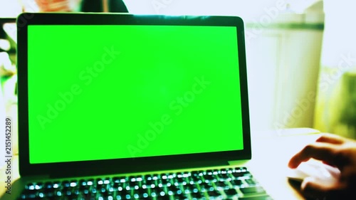 Laptop with Green Screen and Hand in Bright Workspace