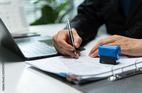 Bild auf Leinwand Businessman completes a printed form with a pen beside a laptop and office stamp, representing documentation, application processing, record keeping, approval, and administrative work