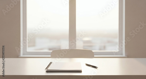 Minimalist desk with notebook and pen by window. Clean office workspace for professional writing, planning, and organized productivity