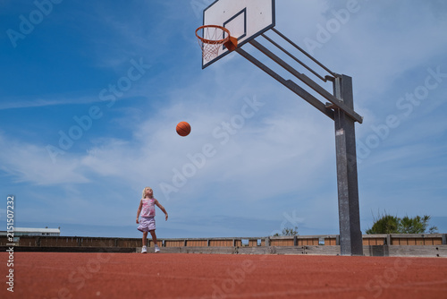 Foto Blonde Toddler Girl Jumping to Shoot a Ball on an Outdoor Basketball Court