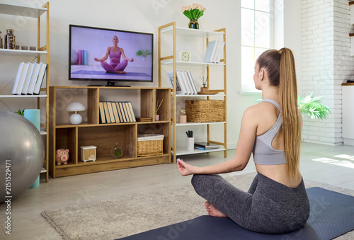 Woman yoga home online fitness tv meditation. She follows a virtual instructor on television, learning breathing and stretches for balanced workout and mindfulness. Calm wellness focus at home
