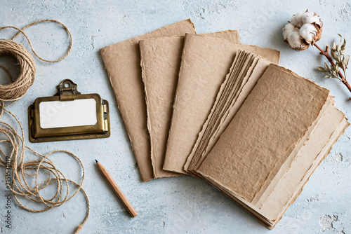 Flatlay of handmade kraft paper notebooks with brass label holder jute twine pencil and cotton flower on concrete table