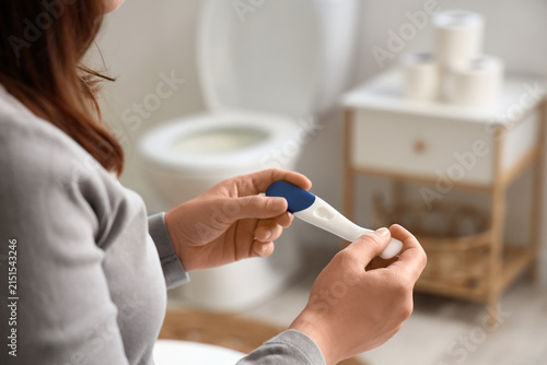 Woman holding a pregnancy test in a bathroom, family planning and fertility c...