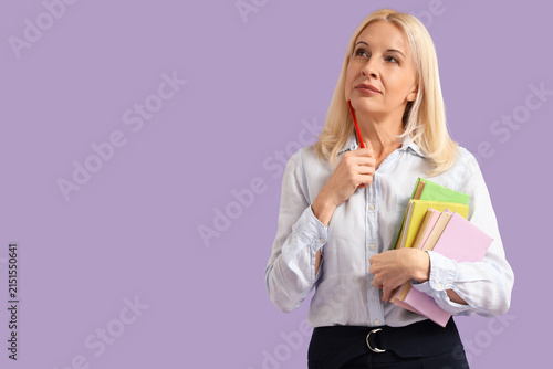 Thoughtful female teacher with books on lilac background