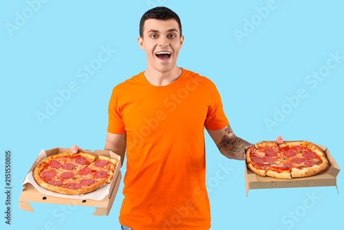 Young man with tasty pepperoni pizza on blue background