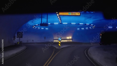 Driving through a Norwegian road tunnel featuring a distinctive underground roundabout and atmospheric blue lighting. The illuminated tunnel interior, road signs and passing traffic showcase Norway's 