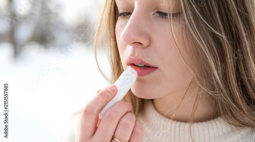 Young woman applying moisturizing lip balm outdoors in winter weather
