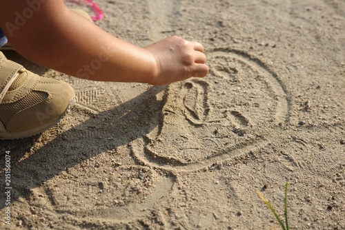 Close-up of a child drawing pictures in the sand with hand wearing sneakers