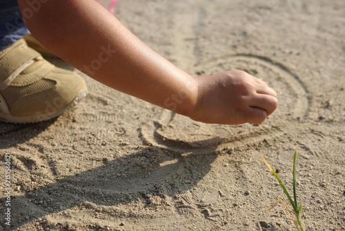 Close-up of a child drawing pictures in the sand on the ground with hand