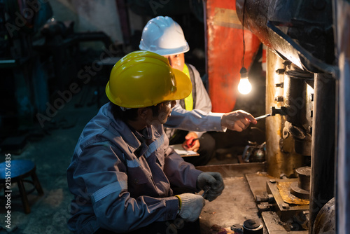 Konstfotografi Senior engineer pointing and instructing technician wearing yellow hardhat during machinery maintenance in factory