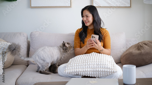Young Asian woman using a smartphone while spending quiet time with her cat at home.