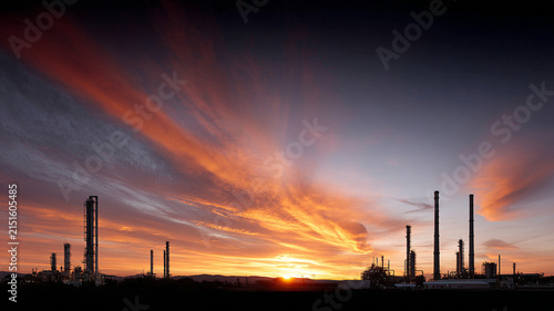 Refinery sunset industrial silhouette smokestack sky cloud horizon, minimal wide shot with orange dusk light over plant
