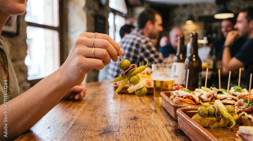 Fototapeta premium Woman holding a traditional Basque Gilda pintxo skewer at a bar counter