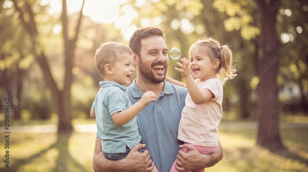 Fototapeta premium Loving father holding up his children near floating soap bubbles