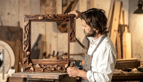 Carpenter holding carved wooden frame in workshop.