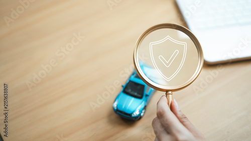 Car insurance concept with an agent reviewing vehicle protection through a magnifying glass and shield icon, symbolizing policy coverage and financial security.