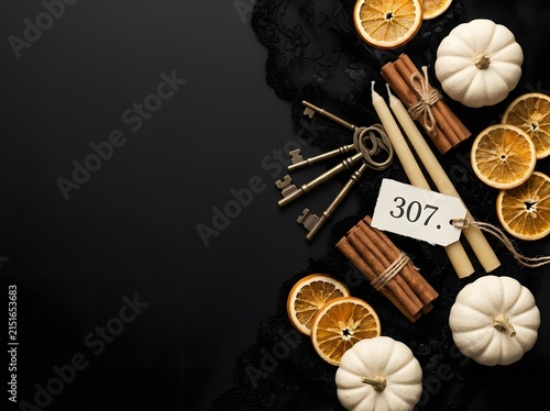 Flat lay composition of white mini pumpkins, dried orange slices, cinnamon sticks, vintage brass keys, and candles on black lace over a dark background with copy space.