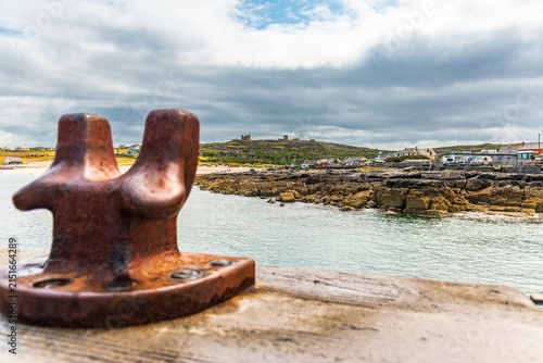 Foto Rusty harbor bollard with Irish coastal village and castle ruins