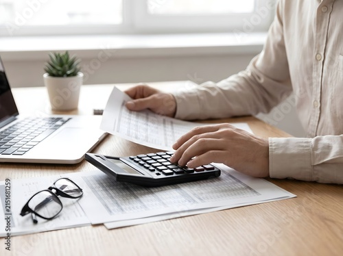 Professional accountant working on financial documents using a calculator at a desk in a bright modern office