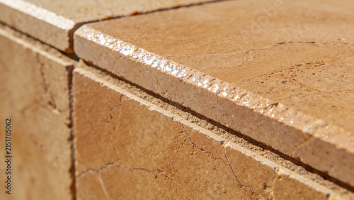 Outdoor beige limestone tile surface with warm sunlight glare and soft leaf shadows