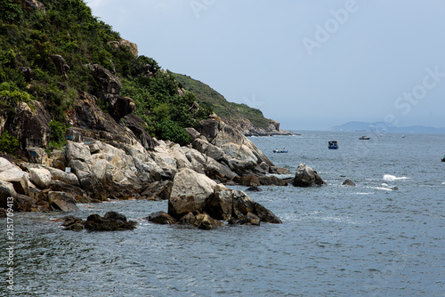 Rocky shoreline with boats near a green hillside on a cloudy day