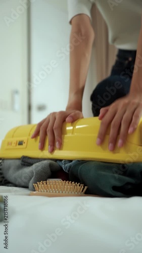 Close-up Stressed young woman struggling to pack an overfilled suitcase before a trip at home. Travel preparation, luggage organization, packing stress. Vacation planning and travel anxiety.
