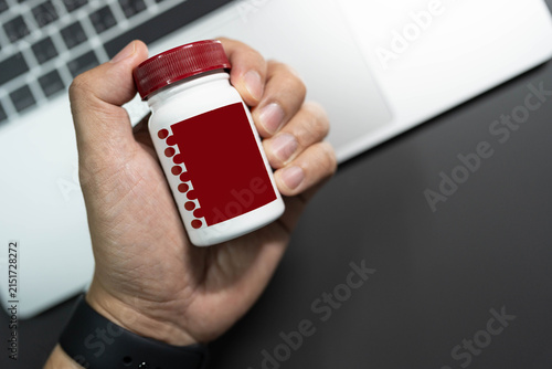 hand holding medicine pill bottle over laptop workspace table concept of workaholic health supplement. office syndrome, stress management, workaholic lifestyle, brain and energy supplements, health 