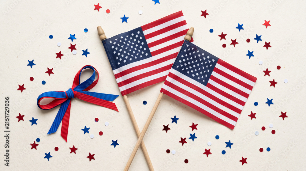 Obraz premium Two small American flags with red and blue star confetti and ribbon on white background.