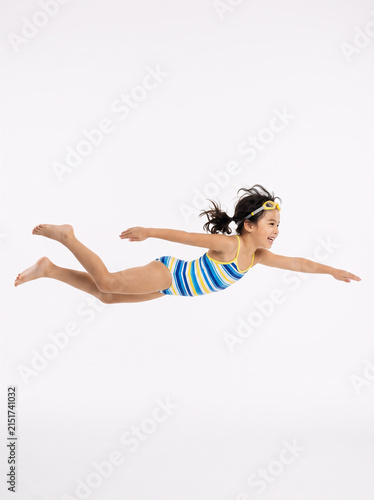 Editorial shot of a child pretending to swim in air, horizontal pose, white background, creative illusion
