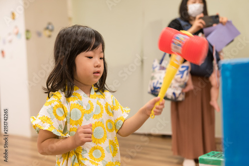 ひまわり柄の甚平を着ておもちゃのハンマーでゲームをする日本人の女の子の幼児