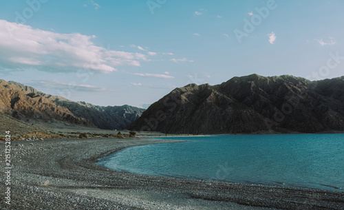 Scenic view of turquoise mountain lake and rocky shore under blue sky with clouds
