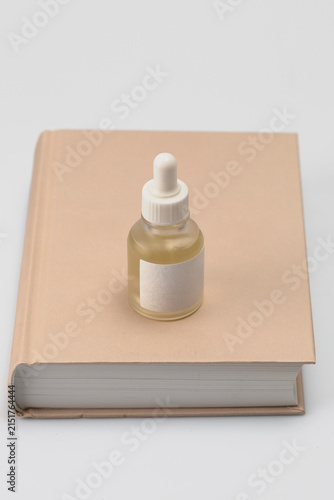 Minimalist skincare aesthetic featuring a glass dropper bottle with golden serum placed on a neutral beige book. Clean studio lighting highlights the elegant simplicity of a modern beauty routine.